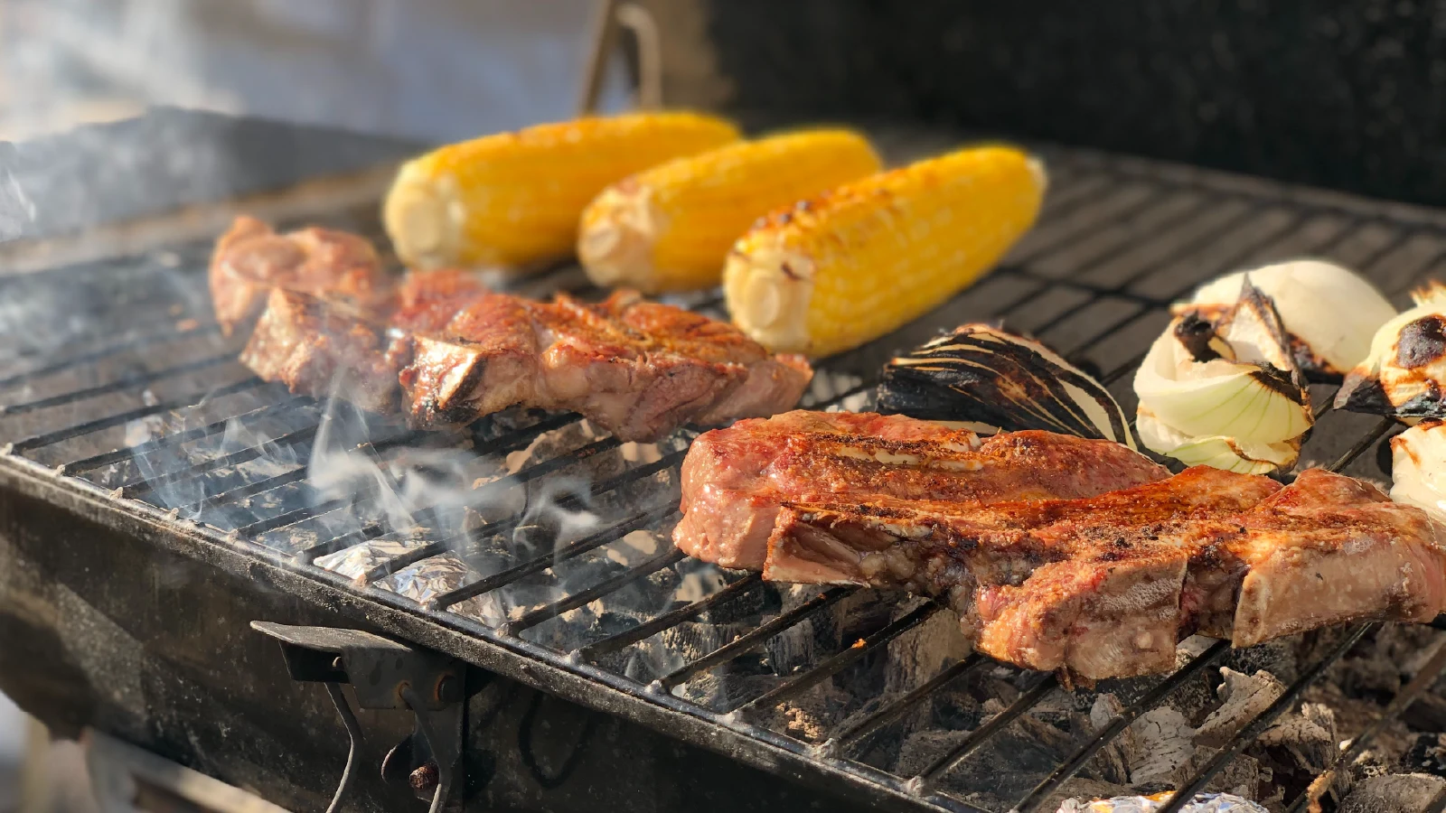 Barbecue grill with steaks, corn on the cob, and onions cooking outdoors at cottage on Pigeon Lake in Kawartha Lakes Ontario