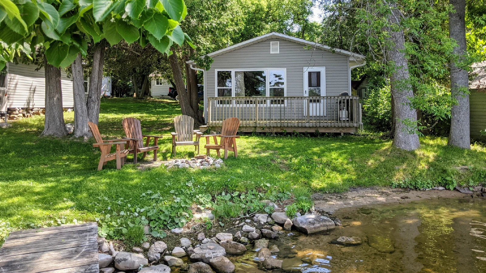 Cottage 1 exterior at Pigeon Lake cottages with private fire pit Adirondack chairs and waterfront shoreline in Kawartha Lakes Ontario