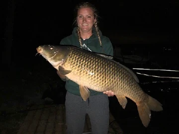 Pigeon Lake Resort Cottage Guest is holding a large fish at night on a dock by a lake.