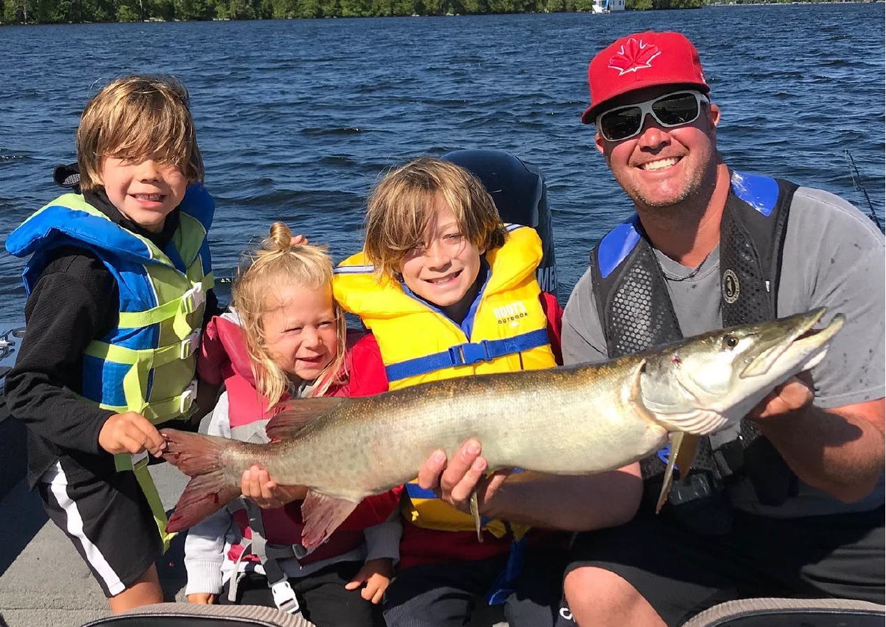Pigeon Lake Resort Cottage Guests.&nbsp; Adult and children wearing life jackets holding a large fish on a boat on a lake.