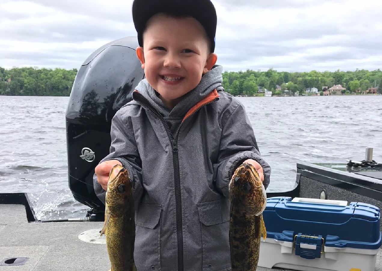 Pigeon Lake Resort Cottage Guest. &nbsp;Child holding two fish while sitting in a boat on a lake.