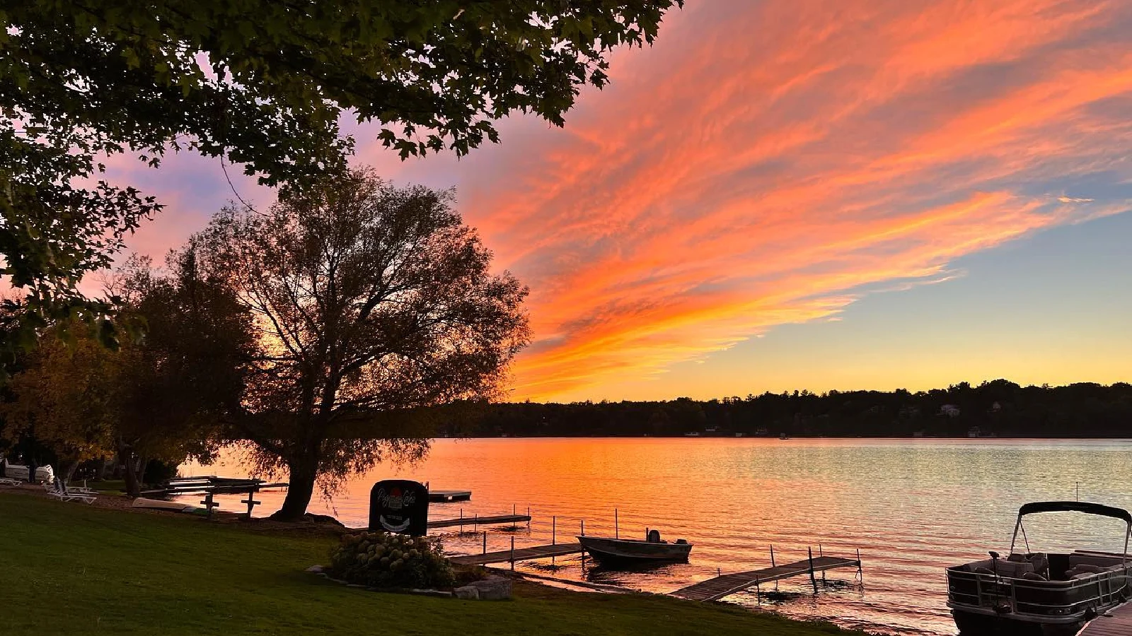 Pigeon Lake sunset with orange and pink sky over calm water, docks and boats along shoreline at Pigeon Lake cottages in Kawartha Lakes Ontario