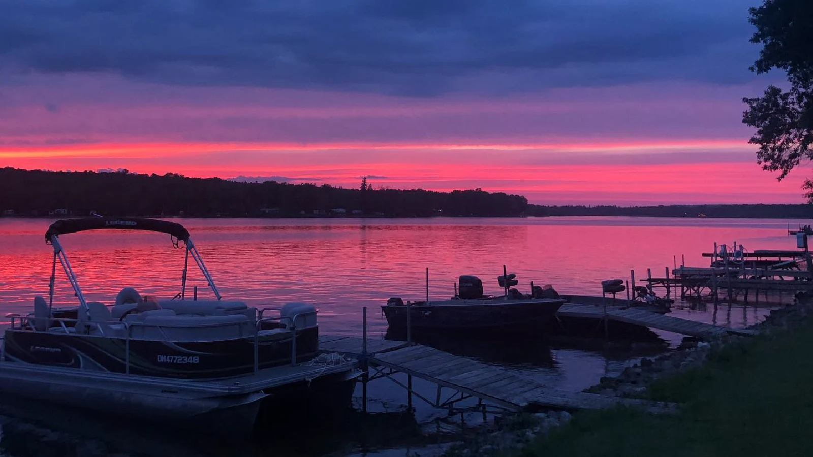 Pigeon Lake sunset with pink and purple sky reflecting on calm water, boats and docks at lakeside cottages in Kawartha Lakes Ontario