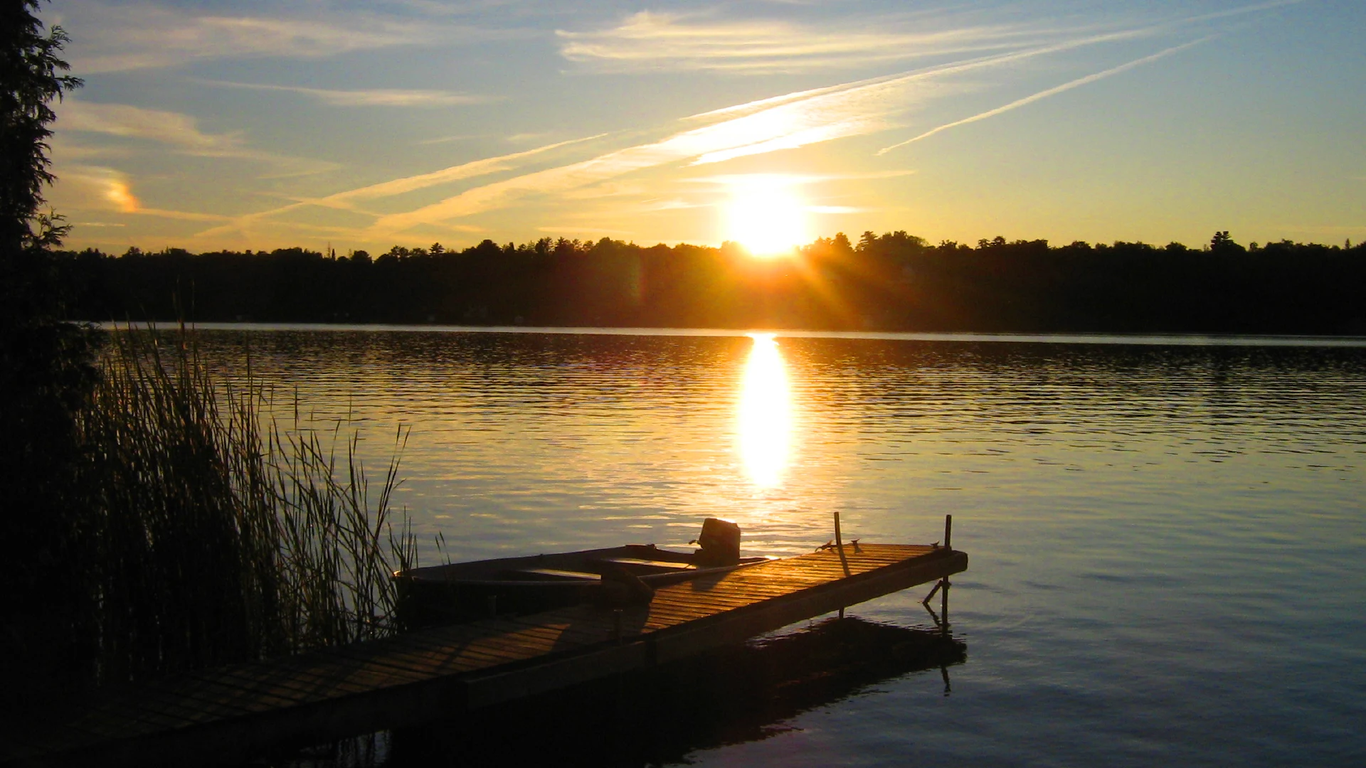 Pigeon Lake sunset with golden sunlight reflecting on calm water and wooden dock at lakeside cottages in Kawartha Lakes Ontario