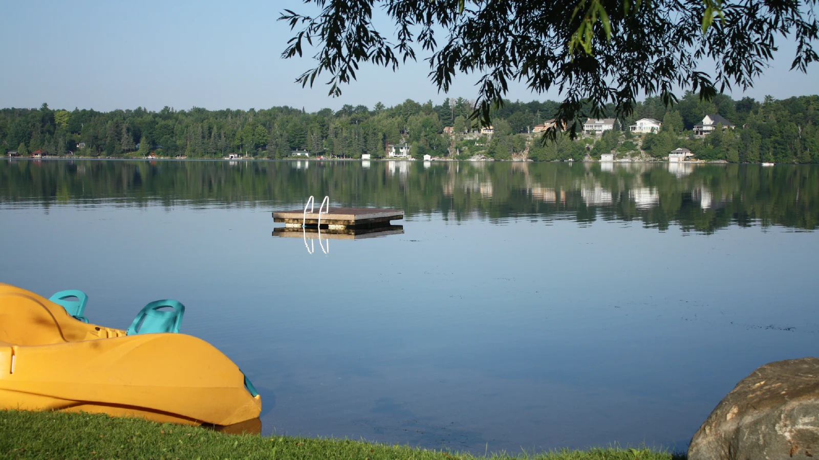 Floating swim platform on Pigeon Lake with calm water, paddle boats, and scenic waterfront views in Kawartha Lakes Ontario