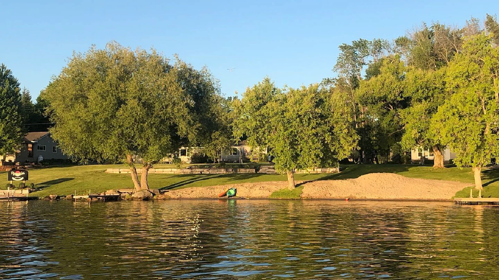 Pigeon Lake Resort sandy beach and swimming area with calm freshwater shoreline, trees, cottages, and waterfront access in Kawartha Lakes Ontario